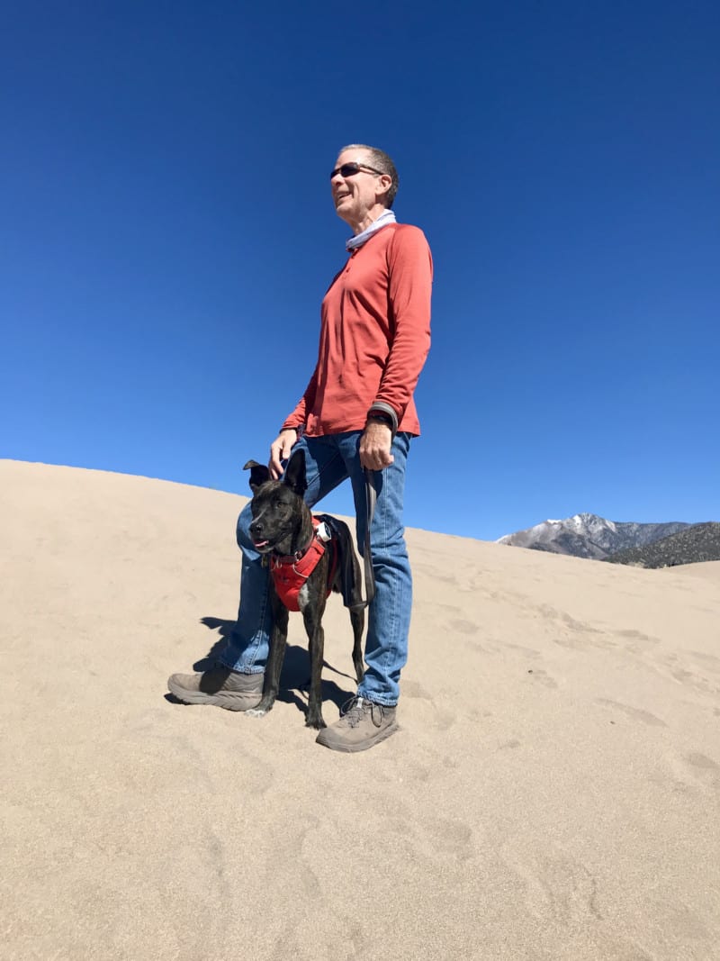A man standing on a dune with a dog between his legs in the Great Sand Dunes National Park