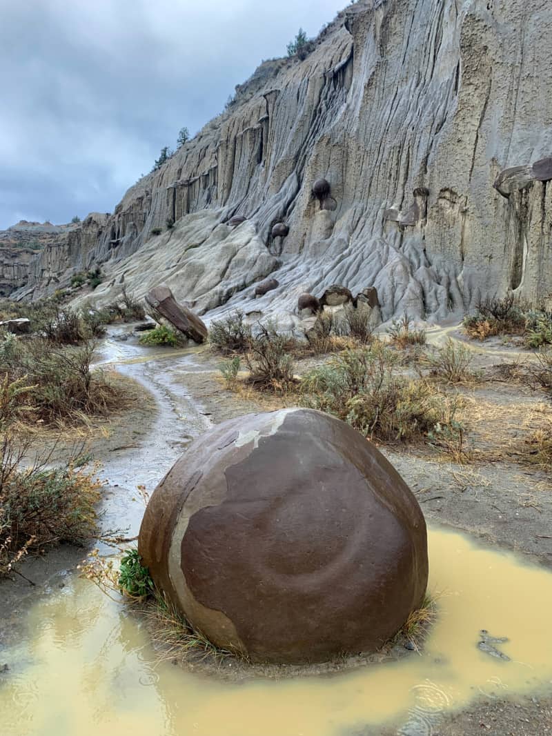 A giant round stone sits in a puddle at the base of a hill in Theodore Roosevelt National Park