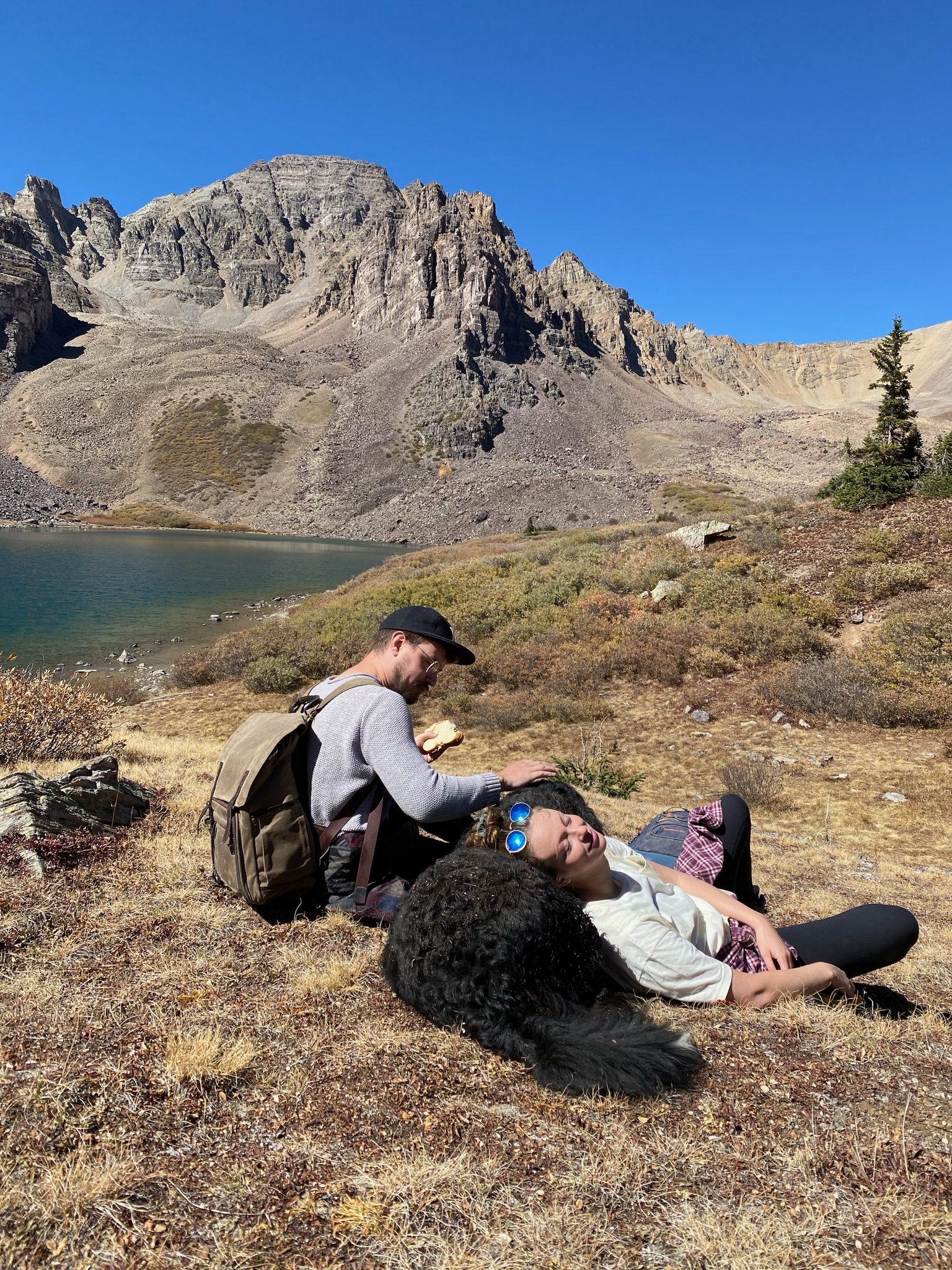 Two people and a dog relax by the Cathedral Lake